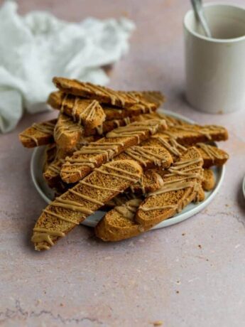 Gingerbread biscotti piled on top of a white plate on a pink background