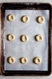 Pressed thumbprint cookie dough on a parchment lined cookie sheet