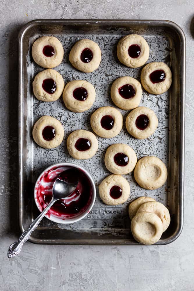Thumbprint cookies filled with jam on a cookie sheet 