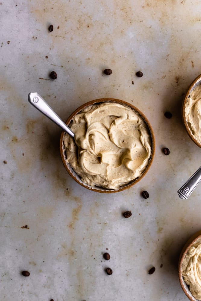 Coffee frosting in a small bowl on a marble backdrop