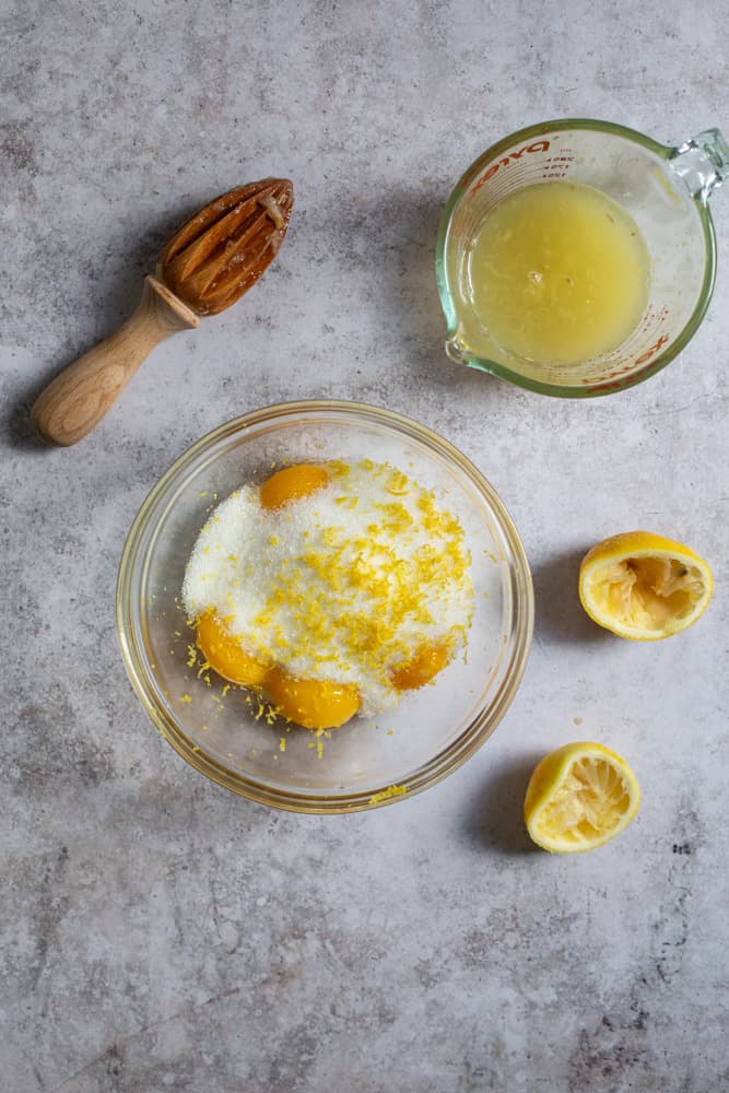Egg yolks, sugar, and lemon zest in a glass bowl on a gray surface