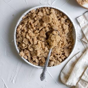 Streusel in a white ceramic bowl with a spoon on a white surface