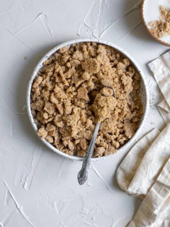 Streusel in a white ceramic bowl with a spoon on a white surface