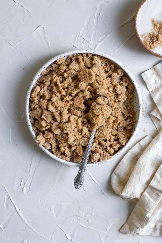 Streusel in a white ceramic bowl with a spoon on a white surface