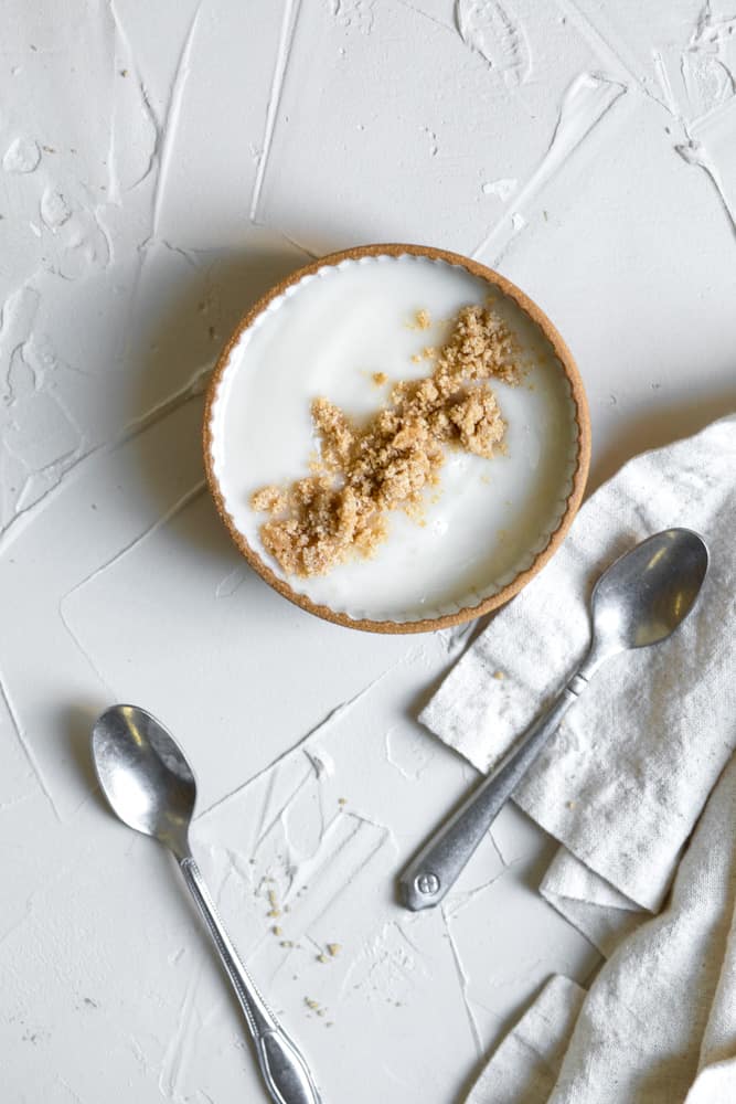 Yogurt topped with streusel in a small bowl on a white surface