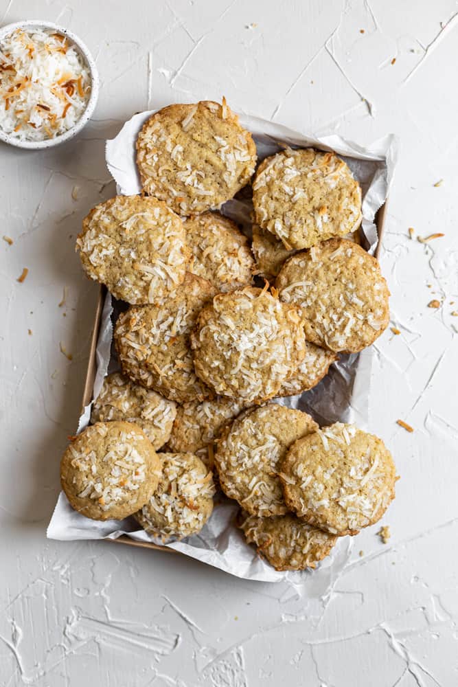 Coconut cookies in a parchment paper lined tray on a white background