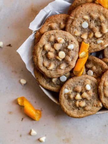 Cookies with orange zest and white chocolate chips in a parchment paper lined bowl on a tan surface