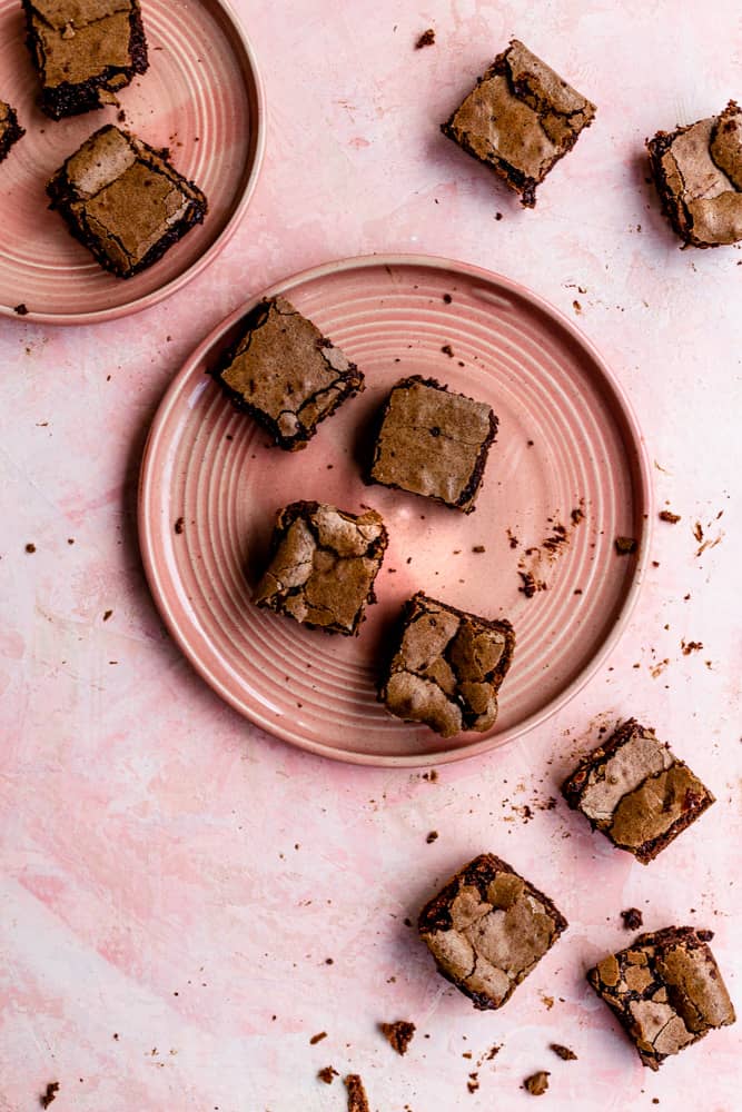 Brownies scattered across a pink plate on a pink backdrop