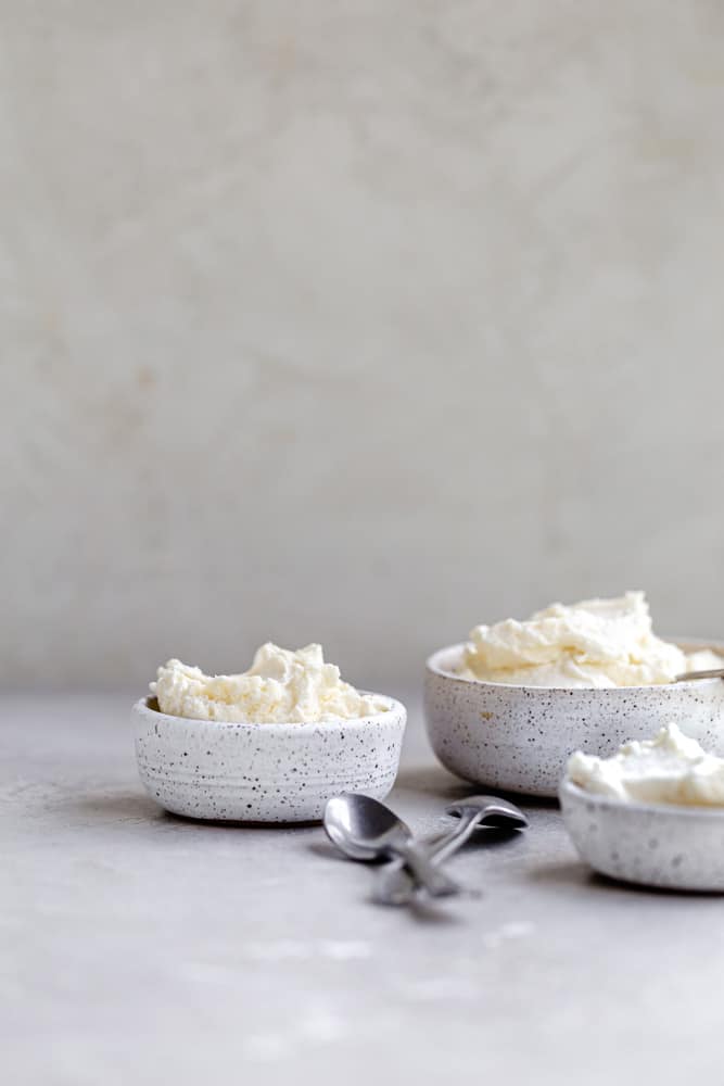 Mascarpone frosting in 3 spotted bowls on a gray surface.