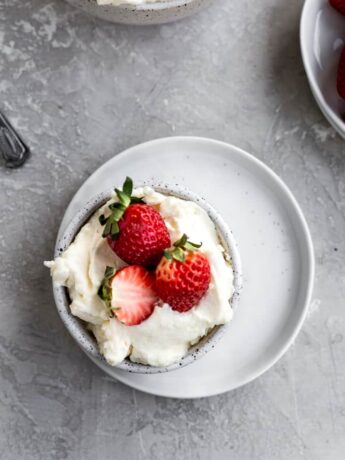Mascarpone frosting in a bowl on a white plate topped with strawberries