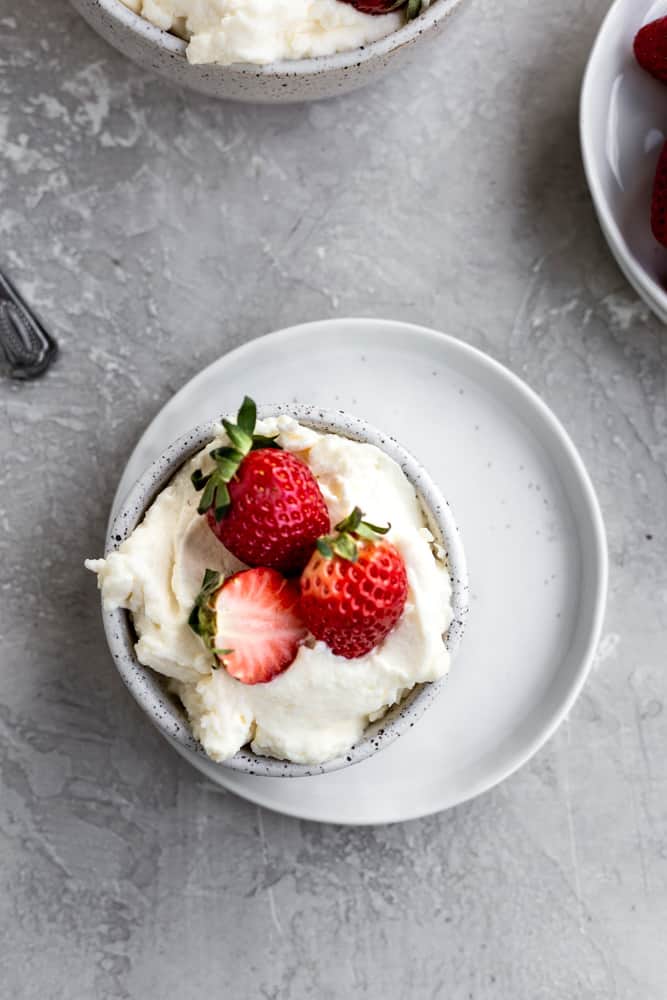 Mascarpone frosting in a bowl on a white plate topped with strawberries.