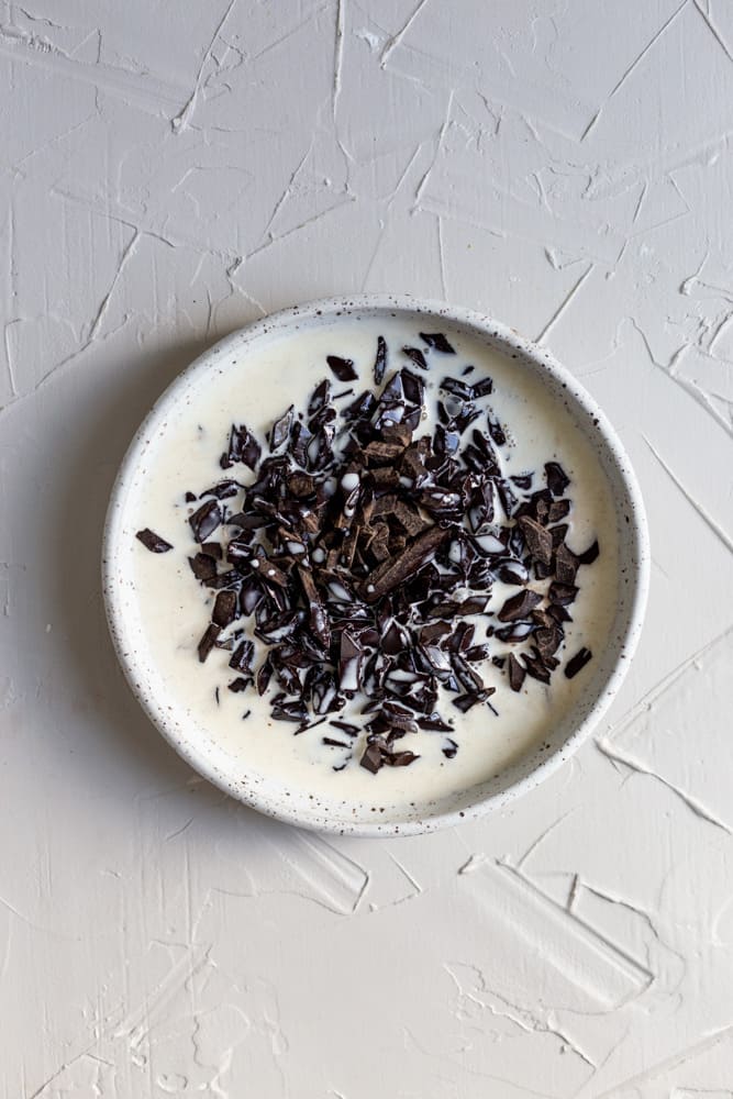 Chocolate and cream in a white bowl on a white surface.