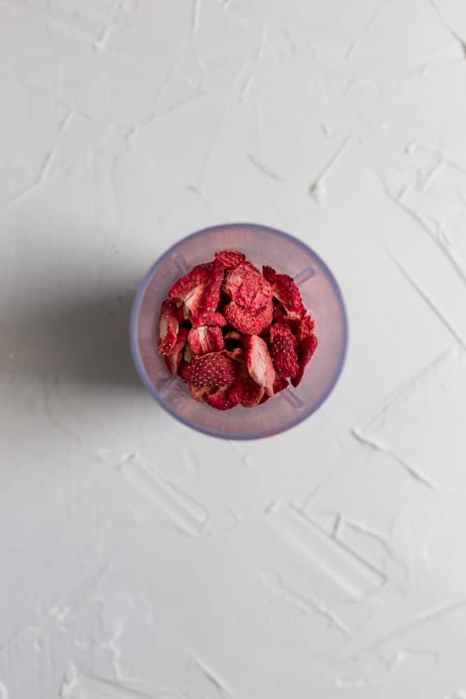 Whole freeze dried strawberries in a mini blender on a white surface