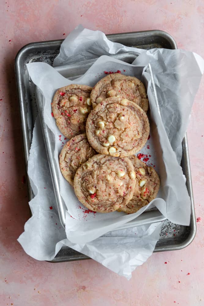 Strawberry cookies layered on trays with parchment paper on a pink surface.