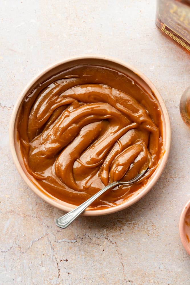 Bourbon caramel sauce in a pink bowl with a spoon inside