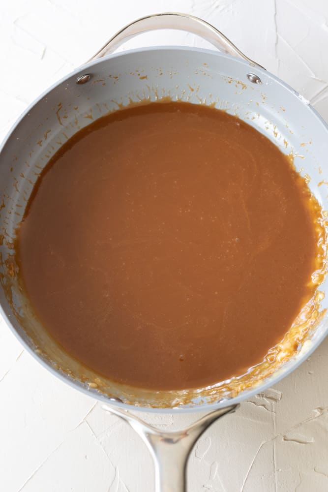 Homemade bourbon caramel sauce in a gray pan on a white surface