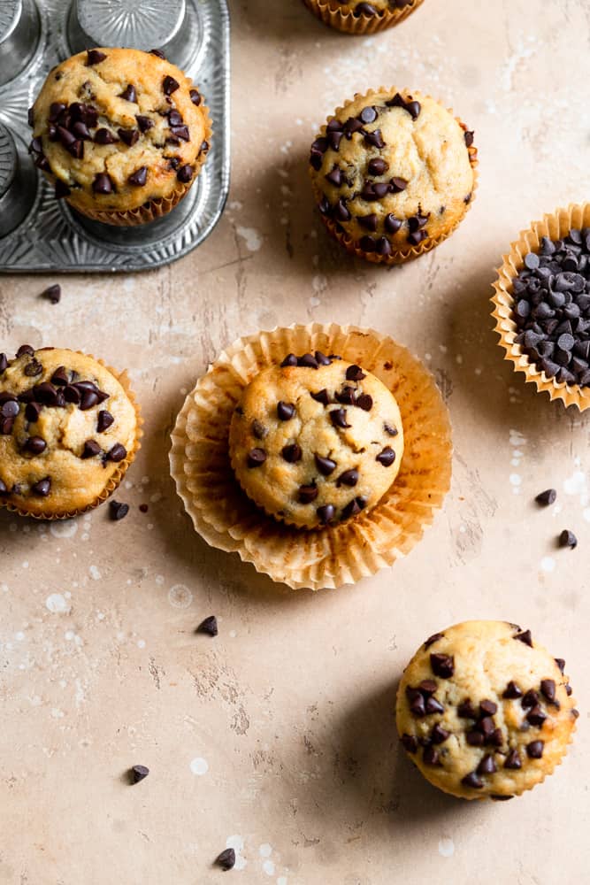 Chocolate chip banana muffins with the liners peeled off on a beige surface