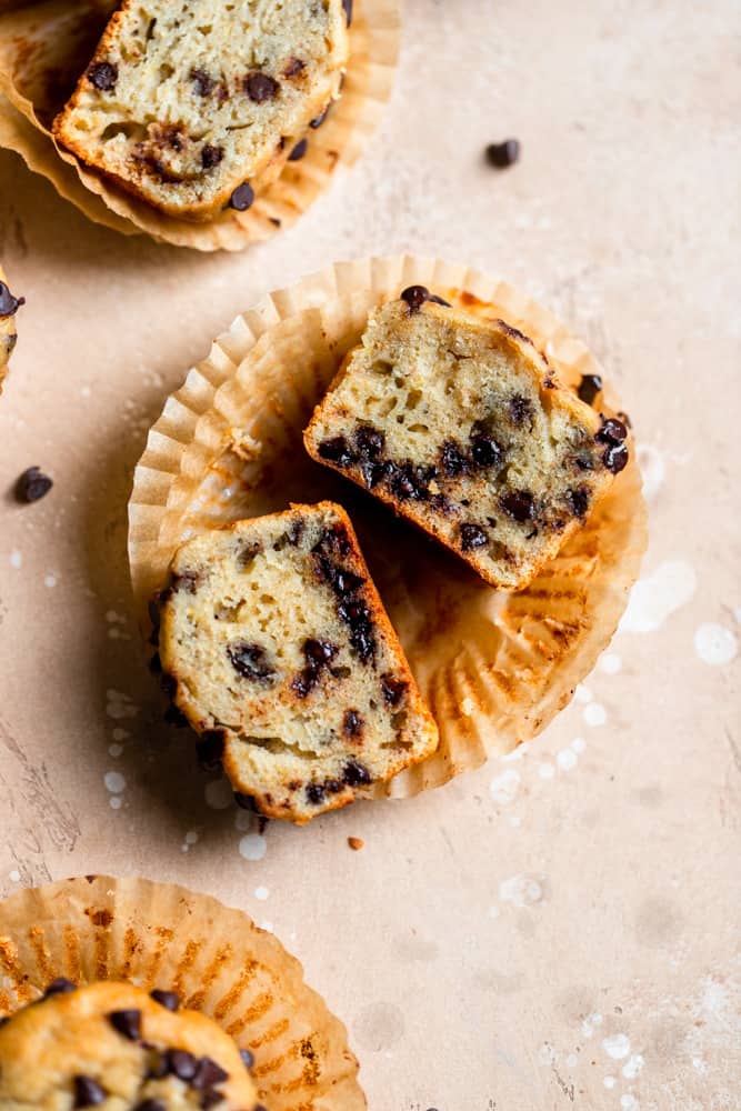 A chocolate chip banana muffin cut in half on a beige surface