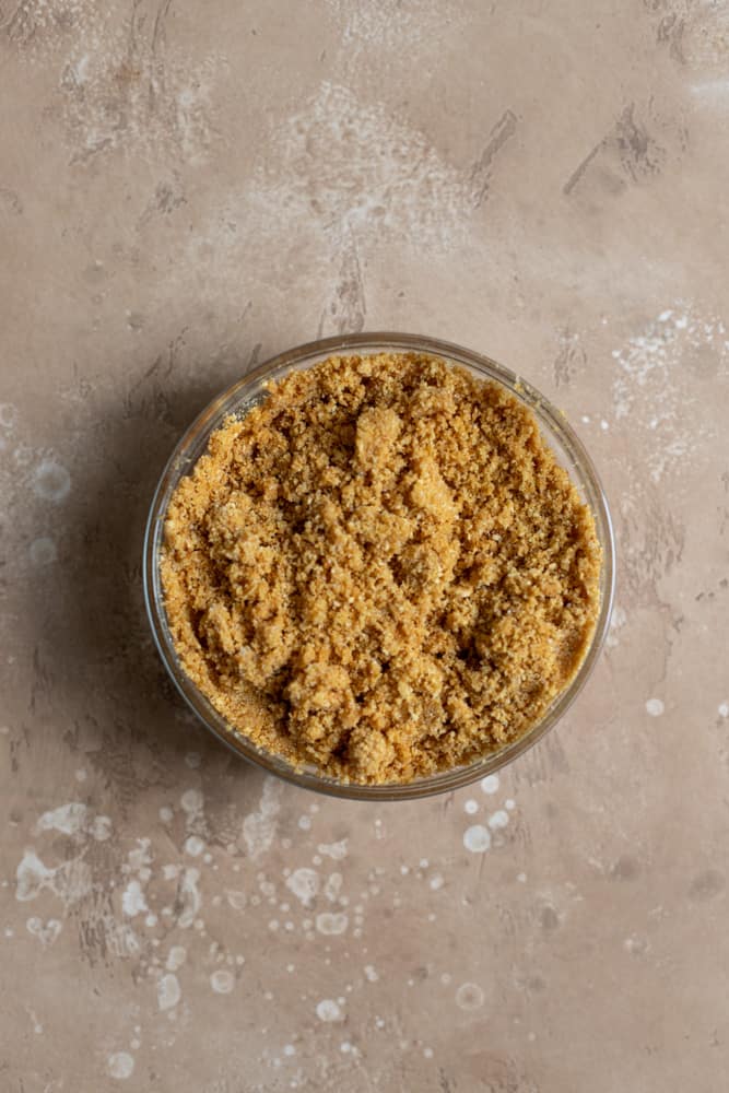 Graham cracker crust in a glass bowl on a beige surface