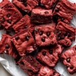 Red velvet brownies pile don each other on parchment paper.