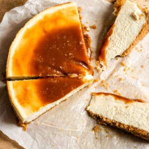 A cheesecake slathered in caramel cut into slices on parchment paper