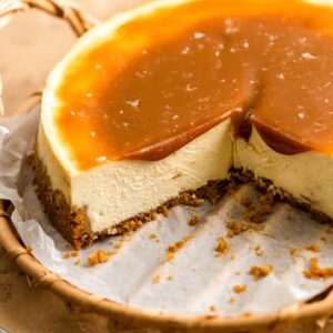 A cheesecake with a slices taken out of it on a wooden tray with caramel sauce on top.