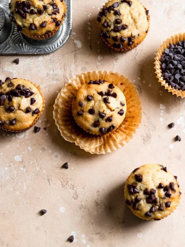 Chocolate chip banana muffins with the liners peeled off on a beige surface