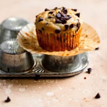 A chocolate chip banana muffin sitting on top of an overturned muffin pan