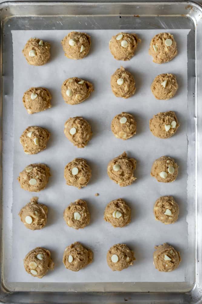 Lots of cookie dough balls on a parchment paper lined sheet tray ready for the fridge.