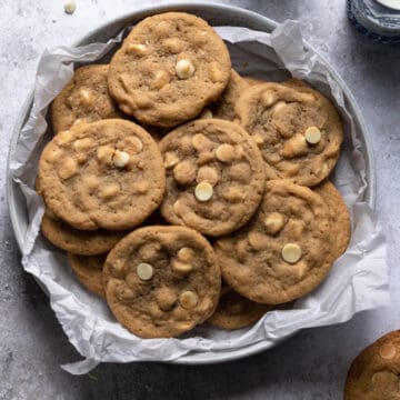 White chocolate chip cookies in a bowl that is layered with parchment paper on a gray textured surface