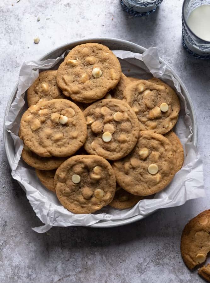 White chocolate chip cookies in a bowl that is layered with parchment paper on a gray textured surface