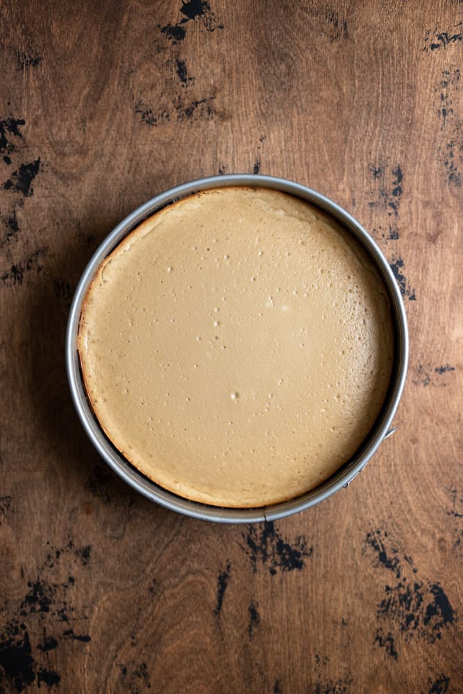 A baked cheesecake still in the pan on a wooden surface.