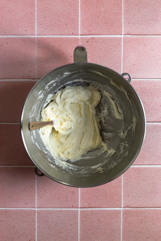 Milk and sugar mixed together in a mixing bowl on a pink tiled surface