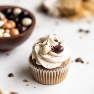 Espresso cupcakes on a white surface next to chocolate covered espresso beans in a bowl