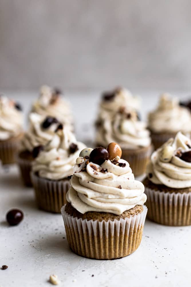 A dozen espresso cupcakes topped with chocolate covered espresso beans on a gray surface
