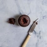 A chocolate cupcake with a hole on it's top with a knife next to it on a blue surface