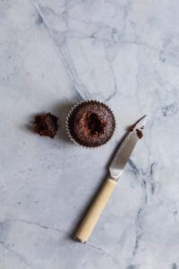 A chocolate cupcake with a hole on it's top with a knife next to it on a blue surface