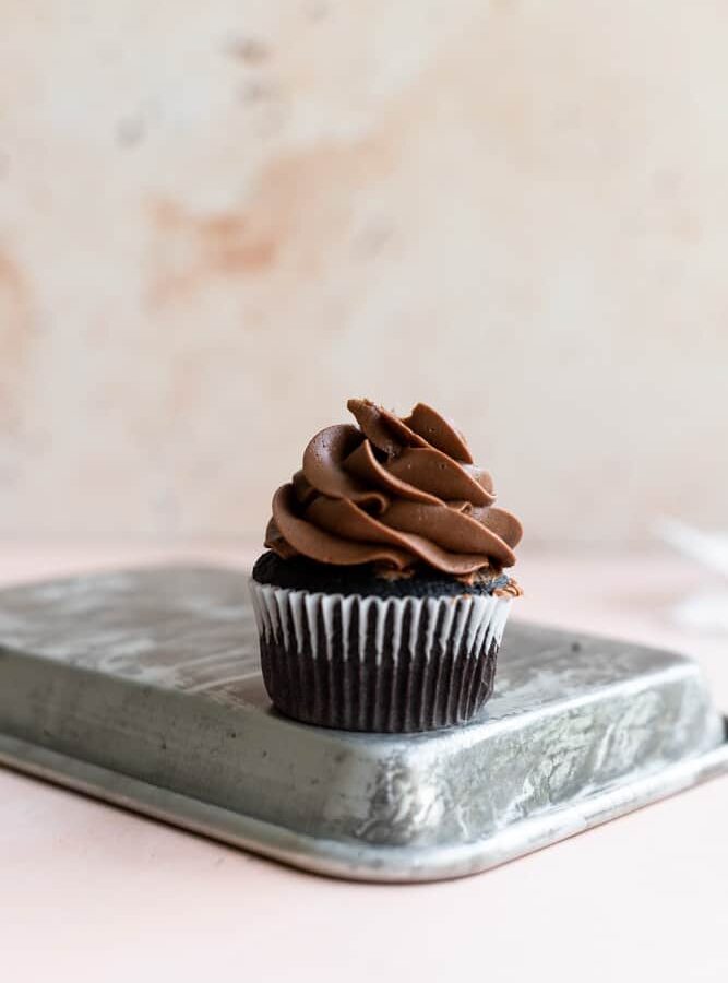 A chocolate cupcake with piped chocolate buttercream on a turned over metal tray.