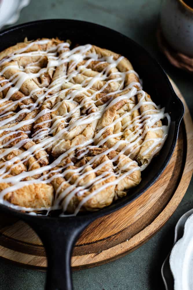 A closeup of cinnamon buns made out of phyllo dough with a cream cheese glaze in a cast iron skillet