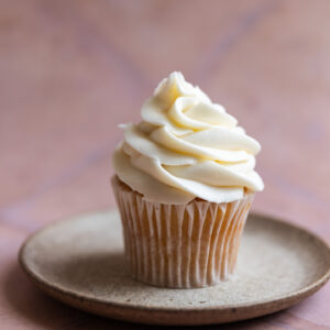 A vanilla cupcake with cream cheese frosting on a stone plate.