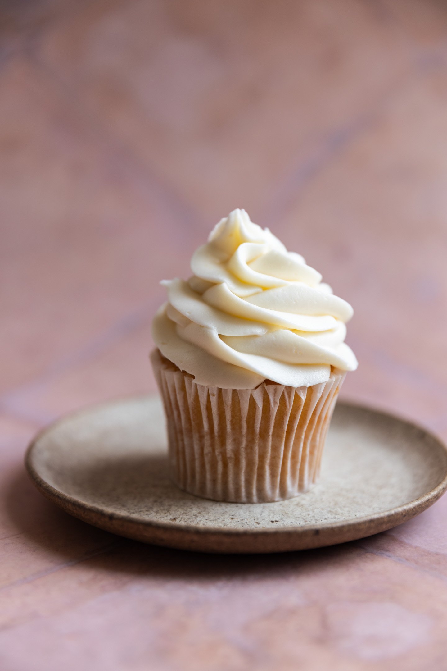 A vanilla cupcake with cream cheese frosting on a stone plate.