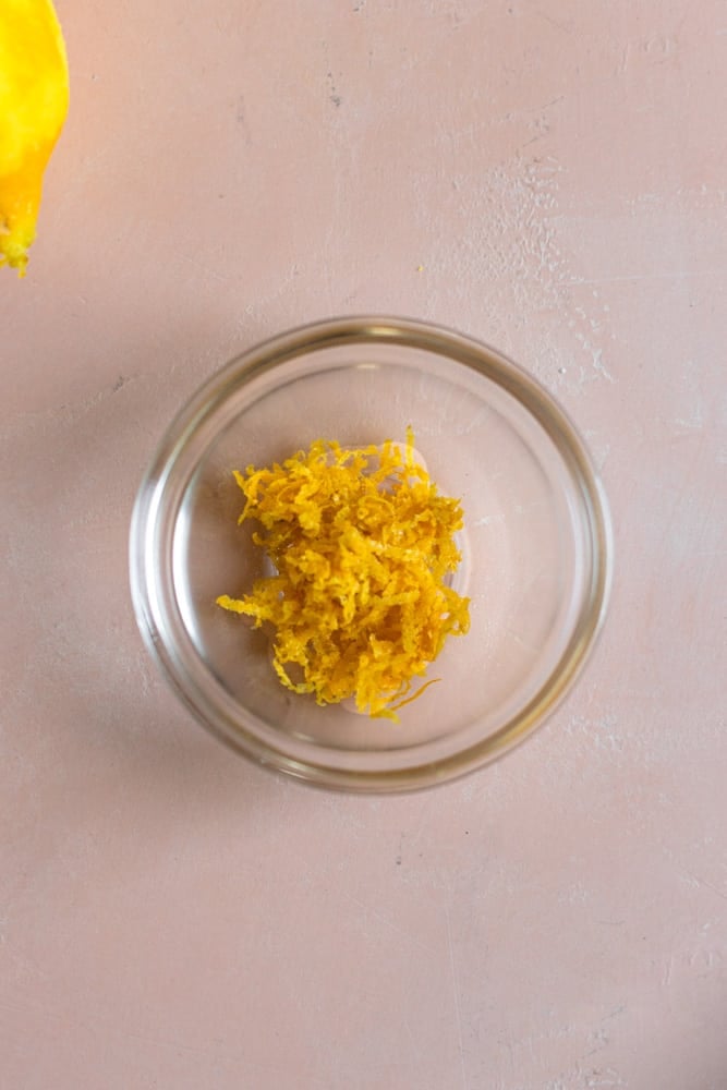 Lemon zest in a small glass bowl on a pink surface