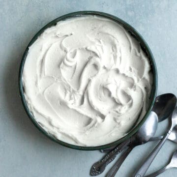 Cream cheese frosting in a bowl on a blue surface with spoons next to it.