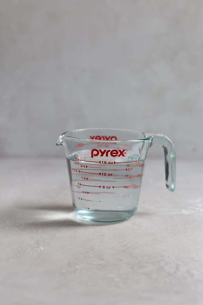 A glass measuring cup filled with water sitting on a gray surface