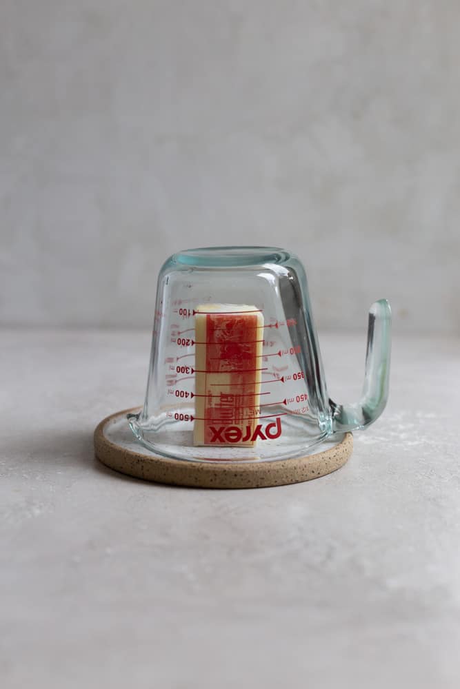 A measuring cup turned over on top of a stick of butter