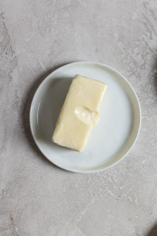A stick of butter softened at room temperature on a small white plate on a gray surface