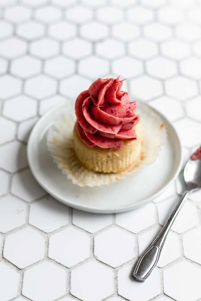 A vanilla cupcake with strawberry buttercream frosting on a hexagonal background