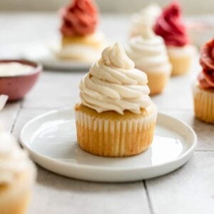 A vanilla cupcake with white frosting sitting on a small white plate