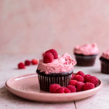 A chocolate cupcake topped with raspberry frosting on a pink plate