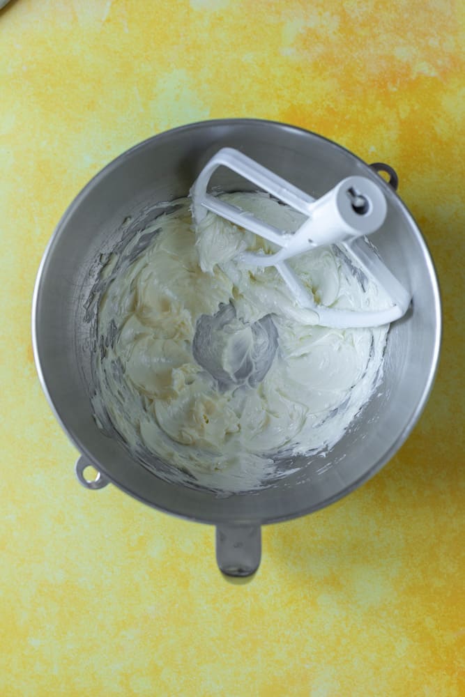Creamed butter in a stainless steel bowl on a yellow surface.